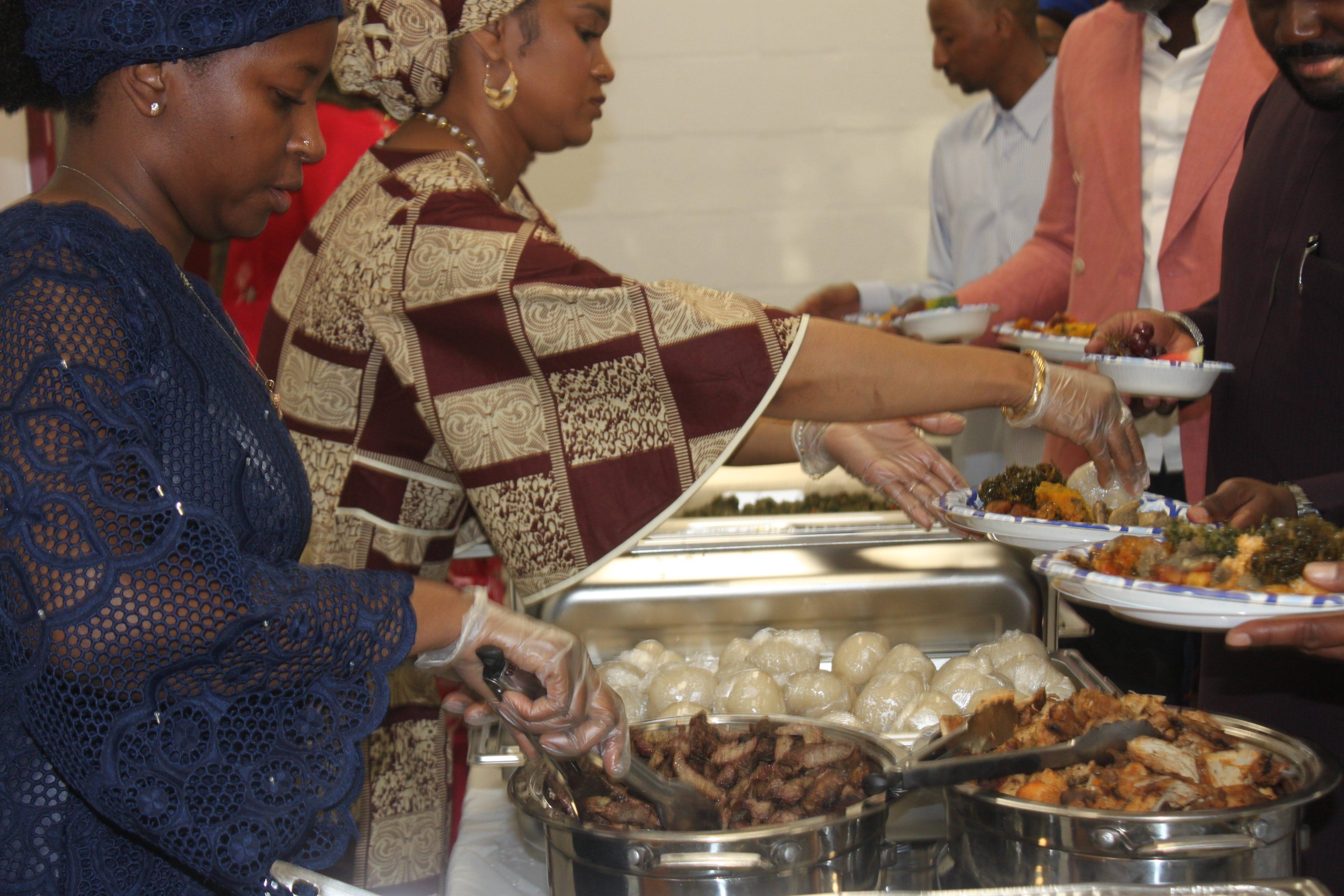 Fulani women in traditional dress serving food to guests at the Al Ada community dinner